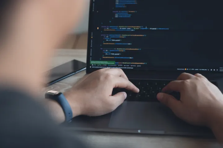 Hände auf einer Laptop-Tastatur, auf dem Bildschirm Programmcode